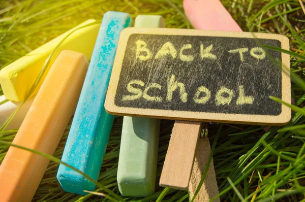 Mini quadro negro escrito Voltar para a escola e giz colorido em um fundo de grama verde — Fotografia de Stock