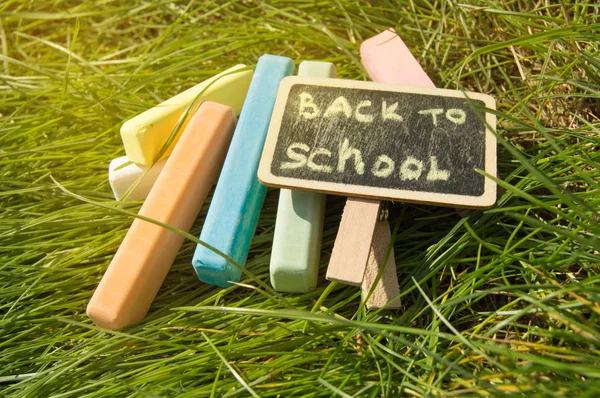 Mini pizarra escrita Volver a la escuela y tiza de colores sobre un fondo de hierba verde — Foto de Stock