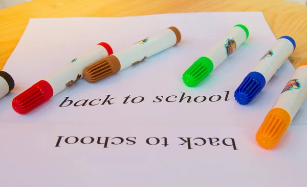 De volta à escola. Uma folha de papel com texto e marcadores coloridos em um fundo de madeira, foco seletivo — Fotografia de Stock
