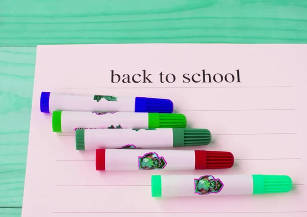 De volta à escola. Folha de papel com texto e marcadores coloridos em um fundo de madeira verde, vista superior — Fotografia de Stock