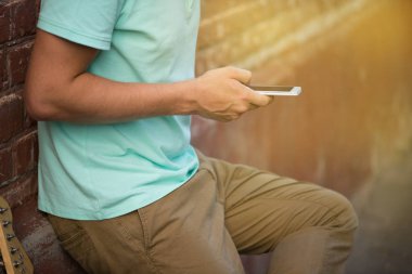 Yaz, parti, genç şık adam kahverengi tuğla duvar yakınında duran, gitar yanında cep telefonu tutan eller, güneş ışığı