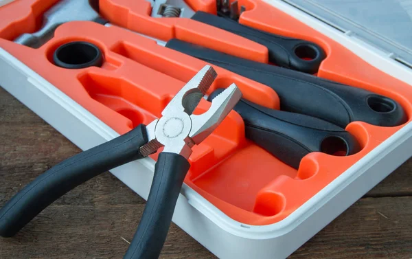 Tool kit pliers, hammer, screwdriver in orange plastic case on old wooden Board with copyspace