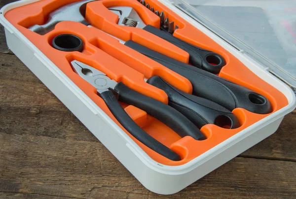 Tool kit pliers, hammer, screwdriver in orange plastic case on old wooden Board with copyspace
