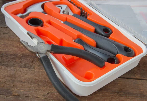 Kit de herramientas alicates, martillo, destornillador en estuche de plástico naranja sobre tabla de madera vieja con copyspace — Foto de Stock