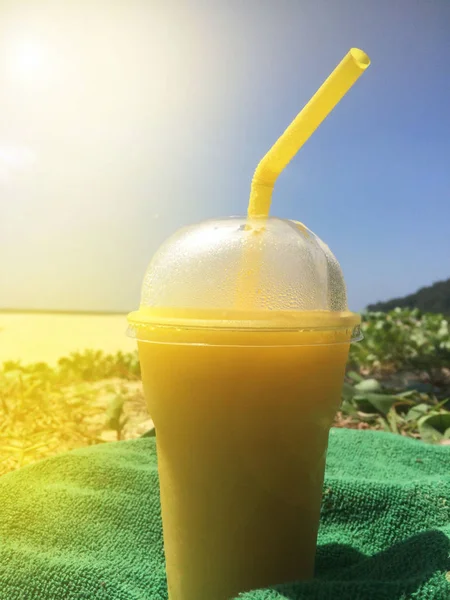 Um copo de coquetel tropical frio de verão com uma tampa enevoada e uma palha fica na praia em uma toalha contra o céu azul e a luz solar — Fotografia de Stock