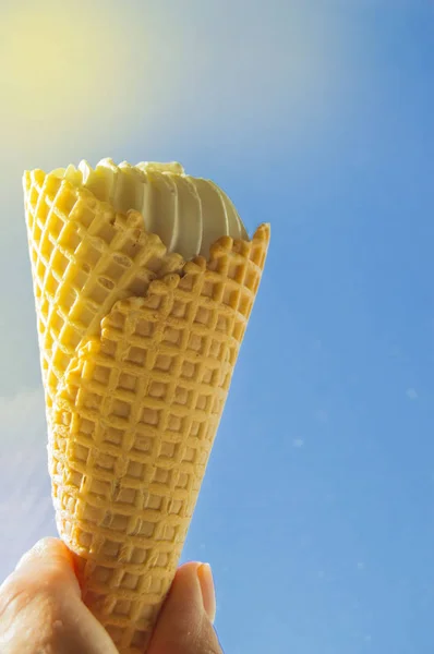 Zomer, feest, hand houden van een vanille-ijsje tegen de blauwe lucht en zonlicht — Stockfoto