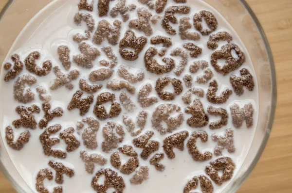 Pohled na misku na mléko, abecední dopisy z cereálií a čokoládové vločky na dřevěném stole, zdravá snídaně pro děti a dospělé, strava — Stock fotografie