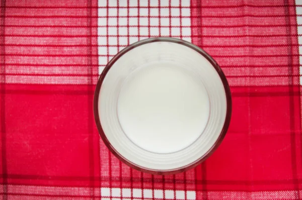 A glass of milk stands on a red checkered cloth, top view