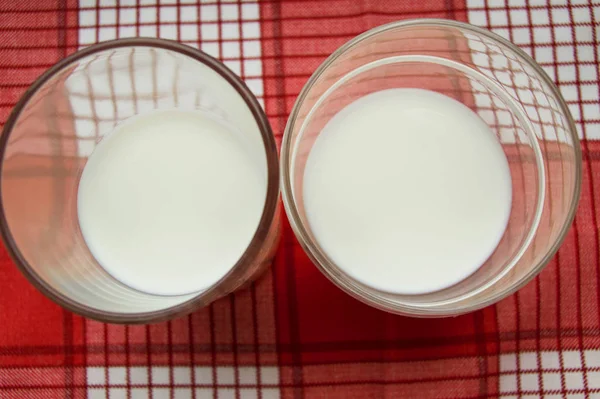 Twee glazen melk staan op een rode geruite doek, bovenaanzicht — Stockfoto