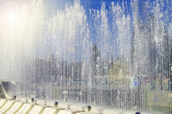 Fuente de la ciudad con chorros de agua y personas al azar, vista a través de salpicaduras en el día soleado de verano —  Fotos de Stock