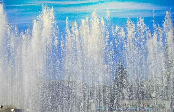 Fuente de la ciudad con chorros de agua y personas al azar, vista a través de salpicaduras en el día soleado de verano —  Fotos de Stock