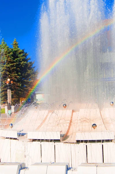 Blurred colorful rainbow on a background of splashing fountain on a Sunny summer day, vertical shot — Stock Photo, Image