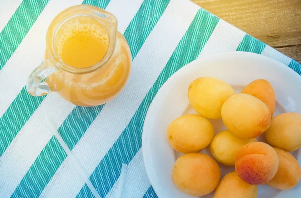Летний напиток и фруктово-свежий абрикосовый сок в стеклянном кувшине и спелые абрикосы на салфетке, вид сверху, открытый — стоковое фото