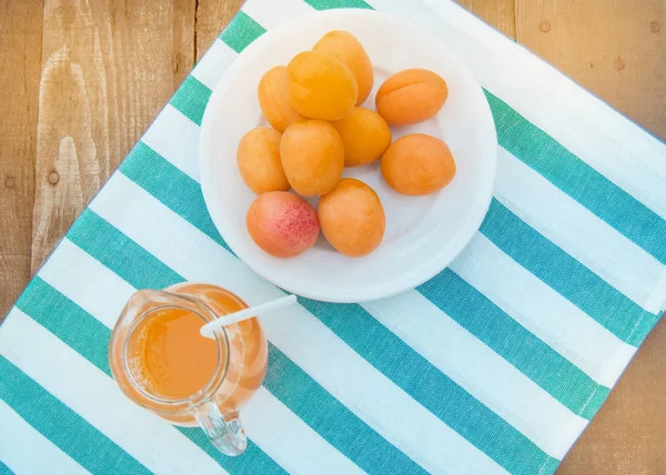 Летний напиток и фруктово-свежий абрикосовый сок в стеклянном кувшине и спелые абрикосы на салфетке, вид сверху, открытый — стоковое фото