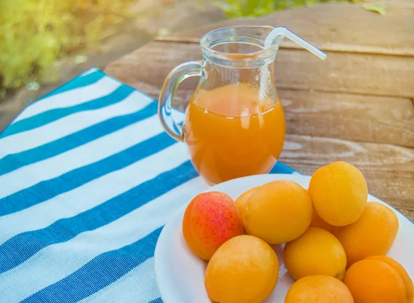 Летний напиток и фруктовый абрикосовый сок в стеклянном кувшине и спелые абрикосы на салфетке, на открытом воздухе в солнечный день — стоковое фото