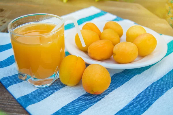 Летний напиток и фруктово-свежий абрикосовый сок в стакане чашки с соломой и спелыми абрикосами на салфетке, на открытом воздухе в солнечный день — стоковое фото
