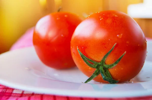 Primo piano di pomodori freschi maturi con gocce d'acqua e un peduncolo verde su un piatto bianco, fuoco selettivo — Foto Stock