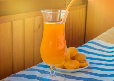 Güneşli bir yaz gününde çizgili bir peçete üzerinde saman ve saman ile cam cam yaz içki-kayısı suyu