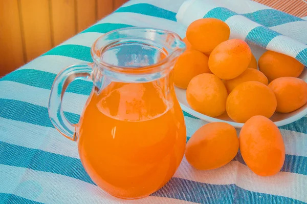 Minuman musim panas - jus aprikot segar dalam kendi kaca, di samping aprikot berada di serbet bergaris — Stok Foto