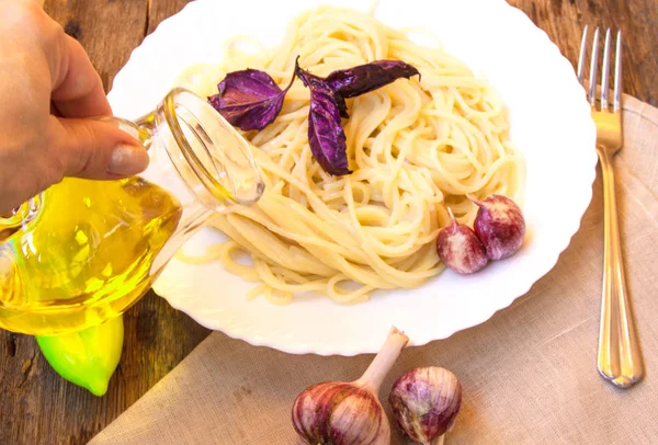 Cucina italiana, spaghetti con basilico e aglio, una mano di donna che tiene una brocca di vetro di olio d'oliva — Foto Stock