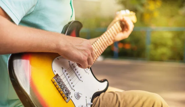 Happy young man hipster sitting playing guitar, close up, summer sunlight, outdoor — Stock Photo, Image