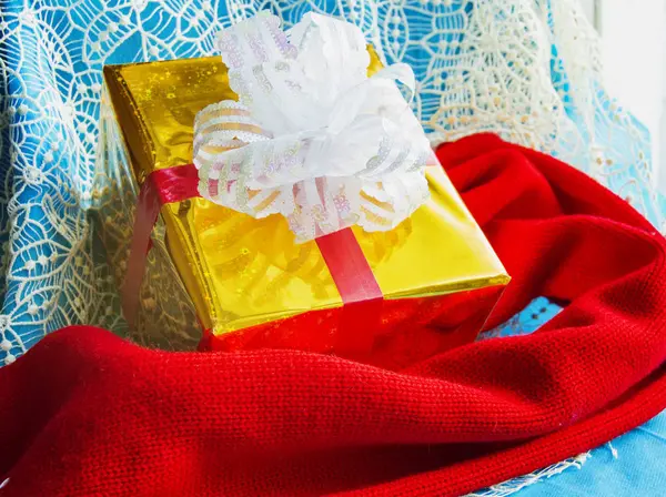 De doos van de gift in goud folie pakket met witte strik en rode gebreide sjaal op mooie blauwe kerst achtergrond, Kerstmis lay-out concept — Stockfoto