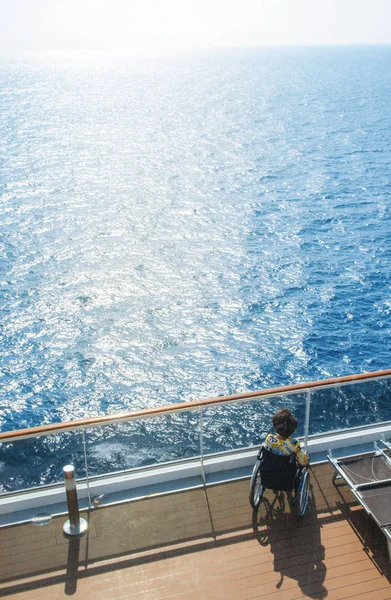 Disabled woman in a wheelchair on the deck of a cruise ship looking at the bright sunlight, the concept of travel accessibility for disabled — Stock Photo, Image