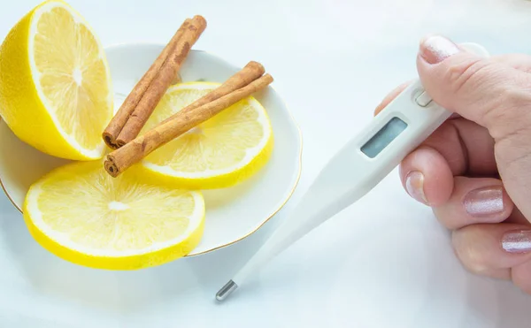 Thermometer in den Händen, Tabletten, Zitrone mit Zimt, das Konzept der Behandlung von Erkältungen — Stockfoto