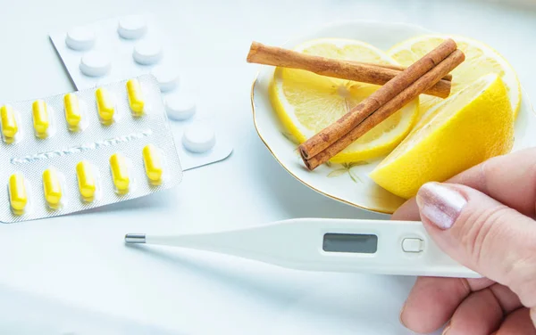 Thermometer in den Händen, Tabletten, Zitrone mit Zimt, das Konzept der Behandlung von Erkältungen — Stockfoto