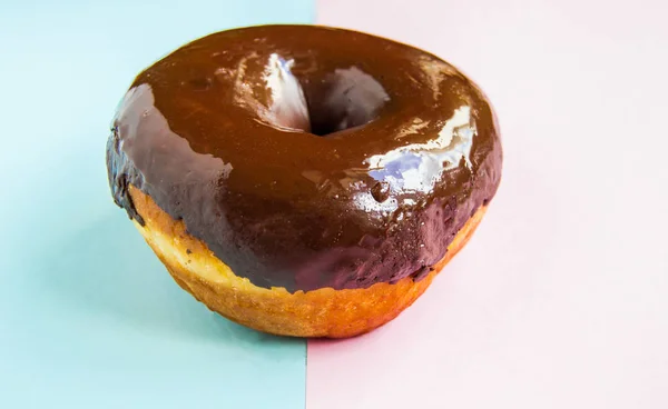 Köstlicher Donut mit glänzender Schokoladenglasur auf pastellrosa-blauem Hintergrund, Nahaufnahme, Seitenansicht — Stockfoto