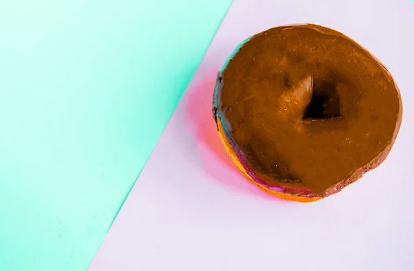 Köstlicher Donut mit glänzender Schokoladenglasur auf pastellrosa-blauem Hintergrund, Nahaufnahme, Draufsicht — Stockfoto