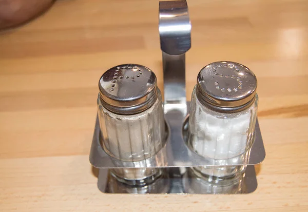 Szklany i metalowy zestaw soli i shakera z pieprzem na drewnianym stole w kawiarni, zbliżenie — Zdjęcie stockowe