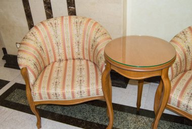 Klasik zarif koltuk ve kavisli bacaklarla küçük bir ahşap masa, Vintage Retro tarzında yapılmış, lüks bir otelin oturma odasında mermer zemin ve duvarlar