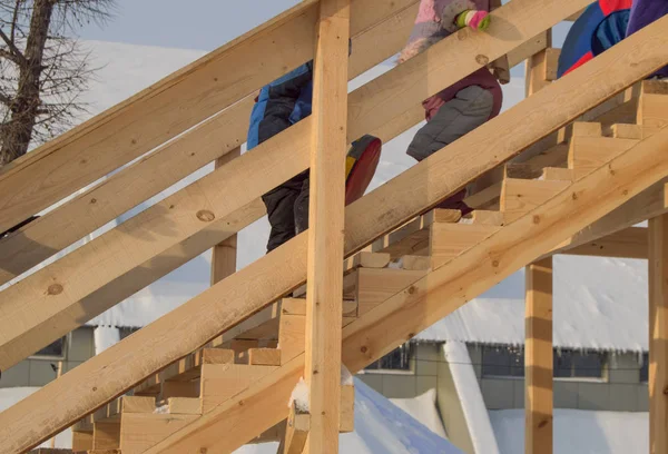 Scivolo in legno per bambini in inverno, bambini con slitte e tubolari scalano la collina, divertimento a Natale — Foto Stock