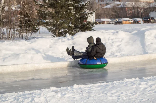 Los niños viajan con toboganes de hielo en un tubo inflable, en tobogán de alta velocidad en hielo resbaladizo, entretenimiento de invierno y actividades al aire libre en el parque de la ciudad — Foto de Stock