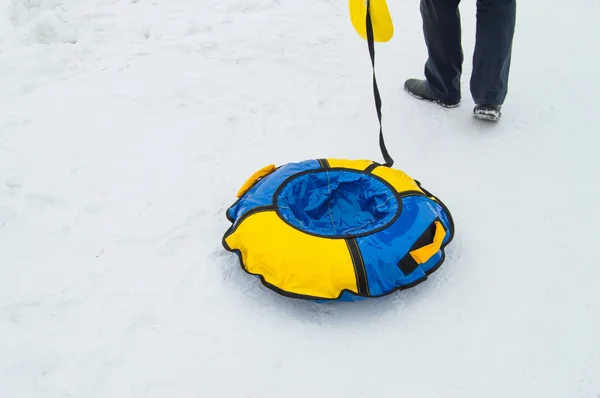 男性の足、冬のアイススライドでスケートのための雪の中で膨脹可能なゴムチューブを引っ張るロープ — ストック写真