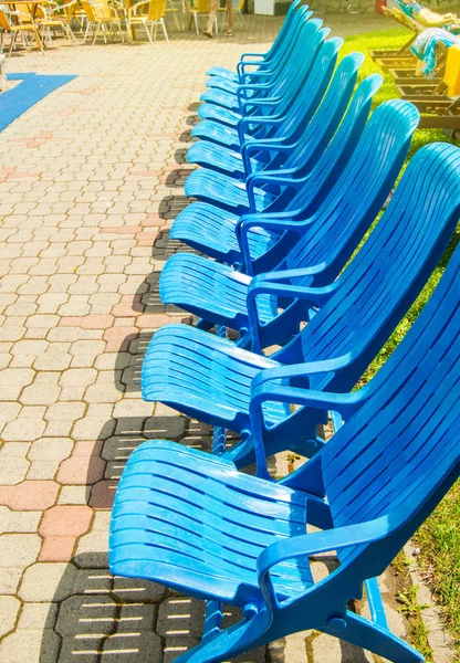 Aire de loisirs d'été au bord de la piscine extérieure, chaises longues modernes vides en plastique bleu se tiennent dans une rangée sur les dalles de pavage par une chaude journée d'été ensoleillée, cadre vertical — Photo
