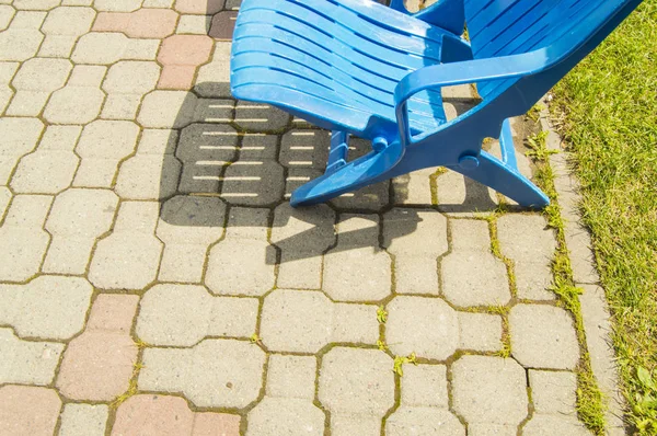 Летняя лоджия у открытого бассейна, современный пустой пластиковый голубой шезлонг, стоящий рядышком на тротуарной плитке в жаркий летний солнечный день, копирующее пространство — стоковое фото