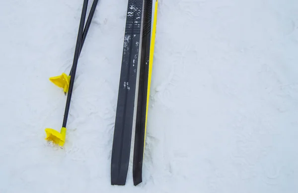 Un par de esquís de fondo negro y bastones de esquí amarillo metálico dejados en la nieve, fondo de invierno con espacio para copiar. El concepto de estilo de vida saludable y activo y deportes — Foto de Stock