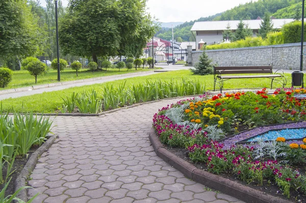 Round flower bed with colorful decorative flowers and plants, garden bench stands on the paving tiles, a beautiful recreation area in the city Park