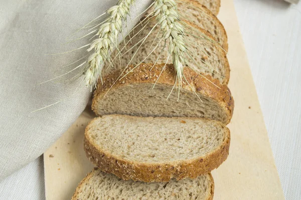 Свежий хлеб на деревянной доске, завернутый в льняную ткань, рядом с пшеничными ушами, копировальное место, вид сверху. Коричневый цельнозерновой нарезанный хлеб, деревенский фон — стоковое фото