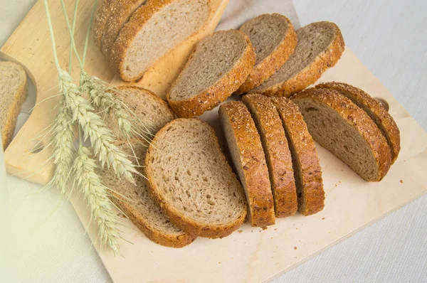 Свежий хлеб на деревянной доске, завернутый в льняную ткань, рядом с пшеничными ушами, копировальное место, вид сверху. Коричневый цельнозерновой нарезанный хлеб, деревенский фон — стоковое фото
