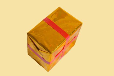 Altın folyo sarı arka plan üzerinde izole kırmızı kurdele ile hediye kutusu sarılı