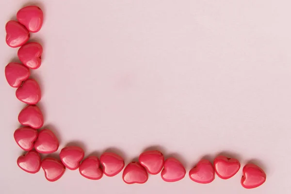 Czerwone koraliki w kształcie serca znajdują się w lewym dolnym rogu na różowym tle, makiety do projektowania — Zdjęcie stockowe