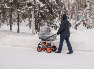 Sıcak giysiler içinde bir adam, bir bebek arabası ile kış Parkı'nda yürüyen bir baba ya da dedesi, mutlu bir aile ve bakım anne kavramı