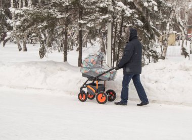 Sıcak giysiler içinde bir adam, bir bebek arabası ile kış Parkı'nda yürüyen bir baba ya da dedesi, mutlu bir aile ve bakım anne kavramı