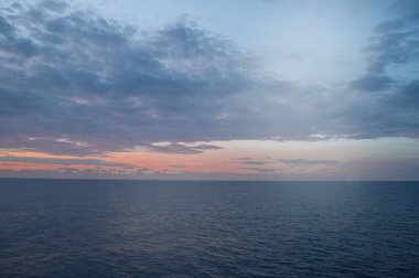 Akdeniz üzerinde sakin gün batımı veya gün doğumu, yumuşak mavi ve pembe bulutlar ile parlayan güneş
