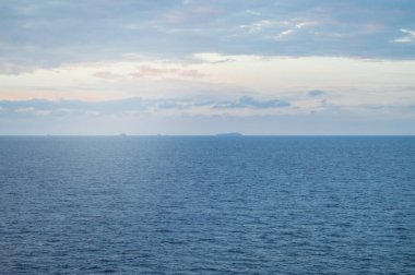 Akdeniz üzerinde sakin gün batımı veya gün doğumu, yumuşak mavi ve pembe bulutlar ile parlayan güneş