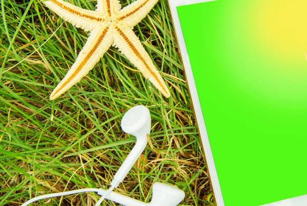 The concept of booking hotels and vacations using a mobile phone, headphones, phone and starfish on the green grass. Chromakey green screen of a mobile phone