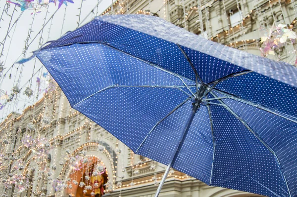 Közelkép egy nyitott kék esernyő kis polka pöttyökkel, az eső a szabadban, szemben a háttérben egy városi utcában — Stock Fotó